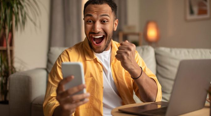 Homem de camiseta amarela sorrindo, olhando para um smartphone na mão e utilizando SVA para provedor de internet.